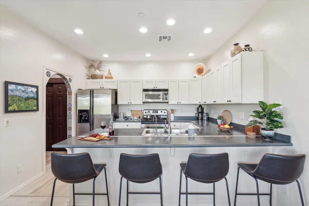 A stylish kitchen with an island and bar stools, stainless steel refrigerator and oven, and thoughtfully arranged decorative items on open shelves. The space feels functional yet warm, designed for both cooking and entertaining guests.