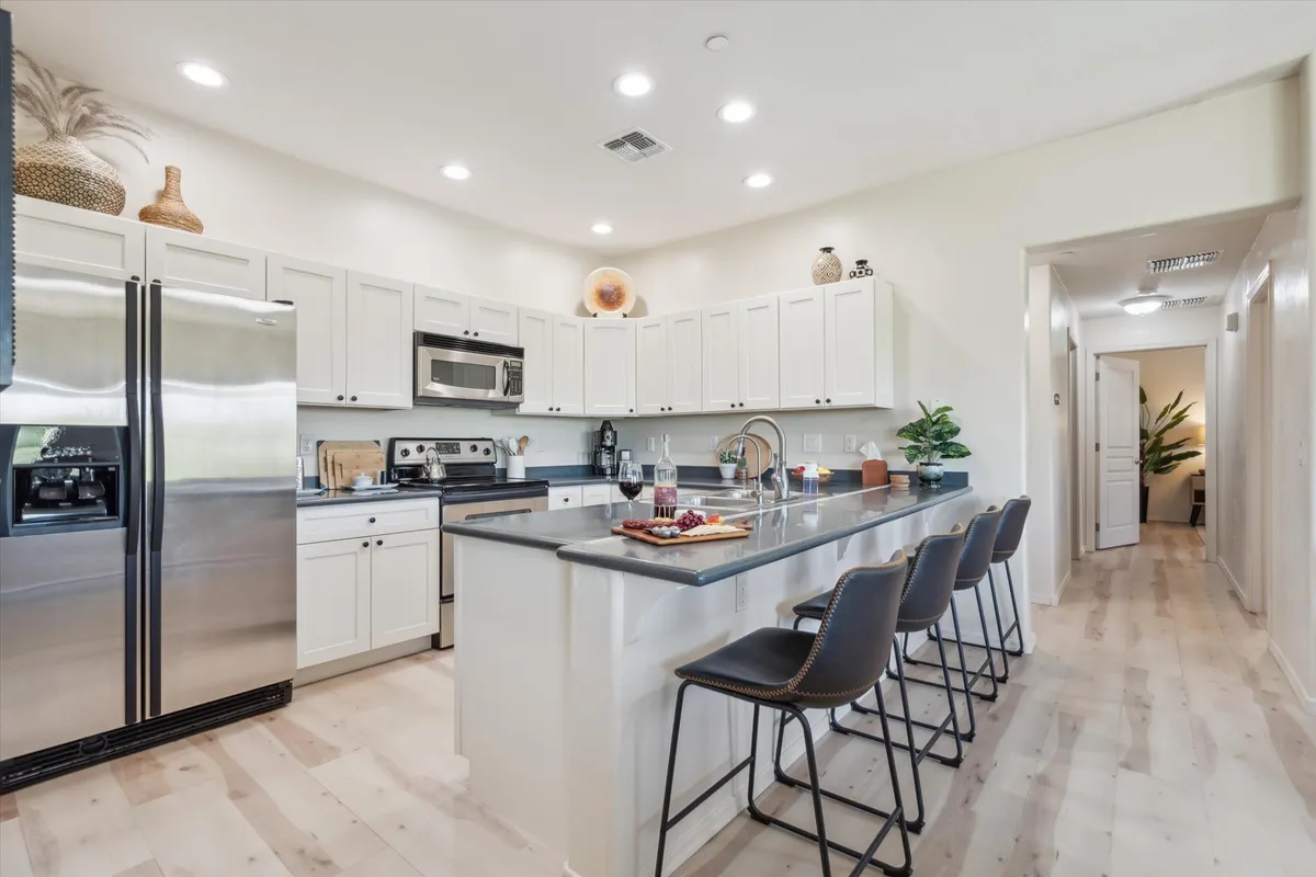 A modern, open kitchen featuring a central island with bar stools, updated stainless steel appliances, and decorative shelving. The layout is spacious, encouraging both culinary activity and social connection, while the bar seating naturally invites guests and family to gather.