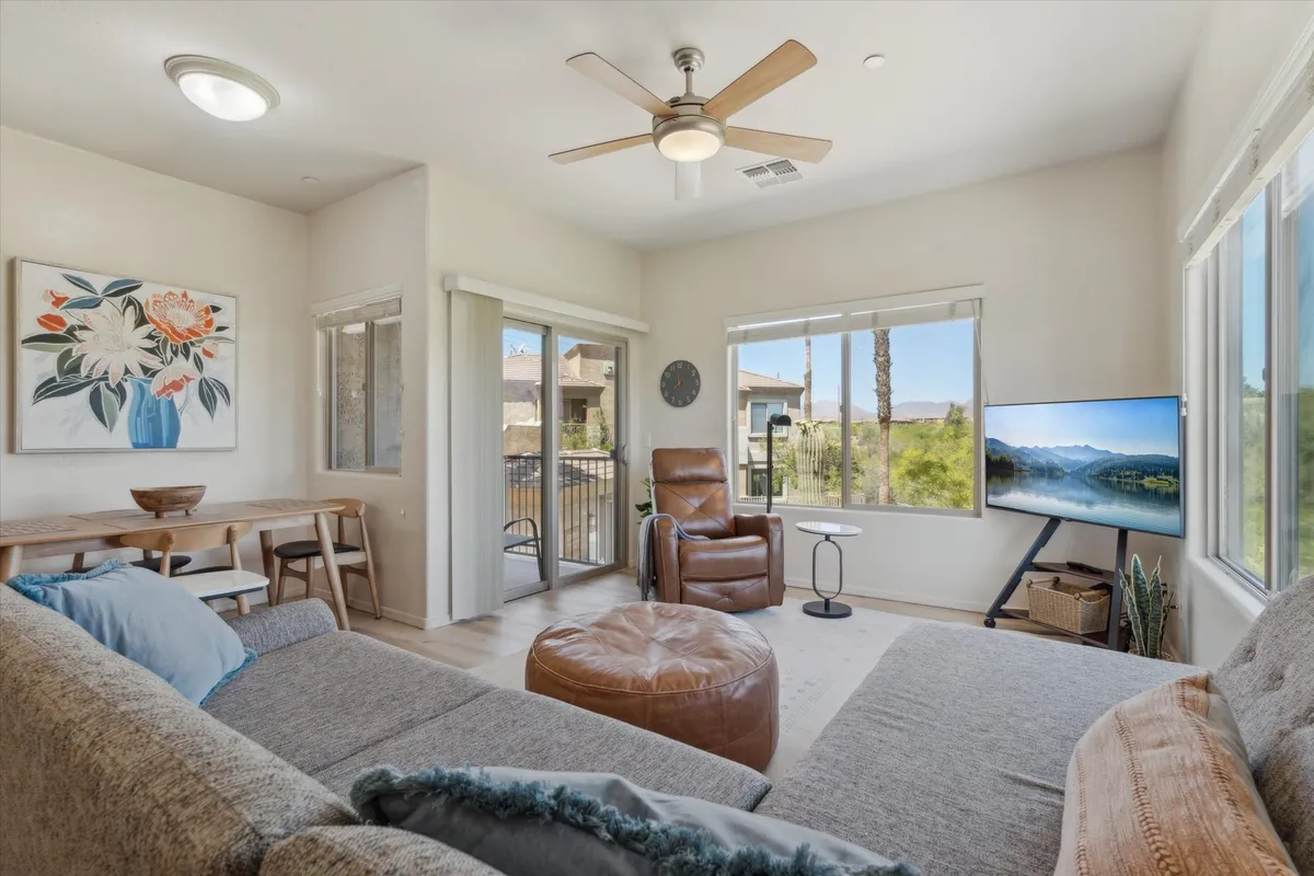 A cozy living room with large windows showcasing scenic outdoor views. The space features a comfortable seating area, decorative artwork, and a welcoming atmosphere. The setup invites relaxation, socializing, reading, or watching television, emphasizing both comfort and the natural setting.